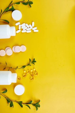 Düz tabaka haplar, balık yağı, yeşil yapraklı vitaminler sarı arka planda, sağlık konsepti, sağlıklı gıda, sağlıklı yaşam için takviyeler, bağışıklık güçlendirici..