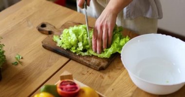 Kadın mutfakta sebze salatası hazırlıyor, tahta kesme tahtasında salata yaprağı kesiyor, sağlıklı gıda konsepti, vegan ya da diyet. Kapat.