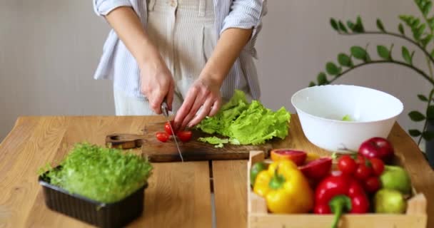 女性はキッチンで野菜サラダを準備しています 木のボード上のトマトを切断 健康的な食品の概念 ビーガンや食事 閉じろ — ストック動画