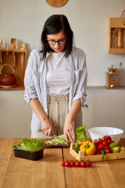 Kadın mutfakta sebze salatası hazırlıyor, tahta kesme tahtasında salata yaprağı kesiyor, sağlıklı gıda konsepti, vegan ya da diyet..