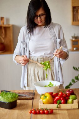 Kadın mutfakta sebze salatası hazırlıyor, salata ve sebzeleri karıştırıyor beyaz kâse, sağlıklı gıda konsepti, vegan ya da diyet.