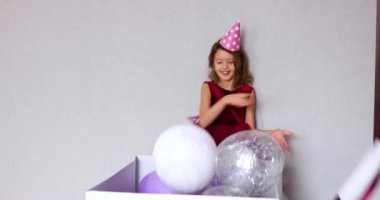 Pembe elbiseli ve şapkalı küçük neşeli kız doğum günü partisinde balonlarla hediye kutusunu açıyor, mutlu yıllar. Kutlama.