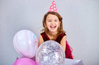 Pembe elbiseli ve şapkalı şirin küçük kız doğum günü partisinde balonlarla oynuyor, mutlu yıllar. Kutlama.