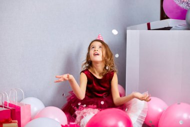 Güzel küçük kız çok renkli konfetileri havaya uçuruyor, evde doğum günü partisinde eğleniyor. Mutlu yıllar çocuğum..