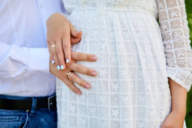 Tanınmayan bir çift, müstakbel ebeveynler, hamile genç bir kadın ve göbeğine dokunan bir erkek mucize bekliyorlar hamile midesi kapanıyor, baharda ya da yaz parkında açık havada.