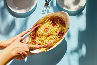 Kadın eli viral fırında domates ve makarna pişiriyor mavi arka planda Fetapasta güneş ışığı, parlak ışık. Yeni, popüler yemek yemeği, Top view, kopyalama alanı.