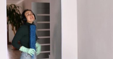 Kulaklıklı kadın dans ediyor ve şarkı söylüyor. Modern evdeki tozları temizlerken, evde oturma odasında, eğlenceli eş günlük temizlik yapıyor..