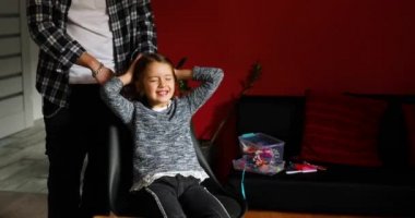 Babası tarıyor, kızının saçını evde tarıyor, çocuk saç çekme hakkında surat yapıyor, kızgın kız acı çekiyor, aile anları yaşıyor, birlikte zaman geçiriyor..