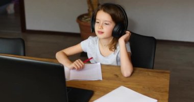 Kulaklıklı şirin kız evde ders çalışmak için dizüstü bilgisayar kullanıyor.