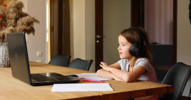 Cute little girl ze słuchawkami za pomocą laptopa do nauki w domu — Wideo stockowe