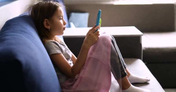 Ragazzina carina seduta sul divano, Kid dipendente dalla tecnologia, godendo di gioco online sul computer tablet digitale — Video Stock