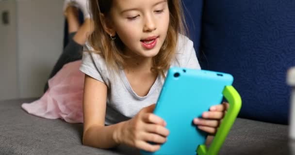 かわいい女の子はソファに横たわって、子供は技術に中毒、デジタルタブレットコンピュータ上でオンラインゲームを楽しむ — ストック動画