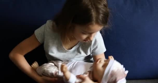 Lille pige sidder på sofaen i rummet derhjemme leger med baby dukke – Stock-video