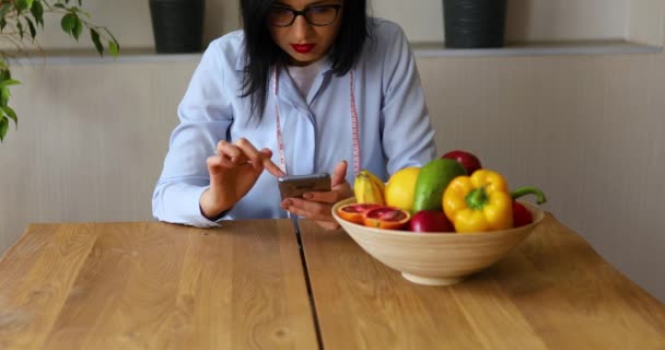 拥有健康水果和蔬菜的营养学家 使用智能手机 正确的营养和饮食观念 女性营养学家 带着水果在家里的办公桌前工作 — 图库视频影像
