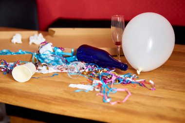 Parti kutlamalarından sonra parti kaosundan sonra parti artıklarını kutlamak için pizza kutusu, boş mavi şişeler, şarap bardağı ve parti süslemeleri olan dağınık ahşap masa..