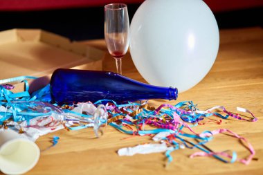 Parti kutlamalarından sonra parti kaosundan sonra parti artıklarını kutlamak için pizza kutusu, boş mavi şişeler, şarap bardağı ve parti süslemeleri olan dağınık ahşap masa..