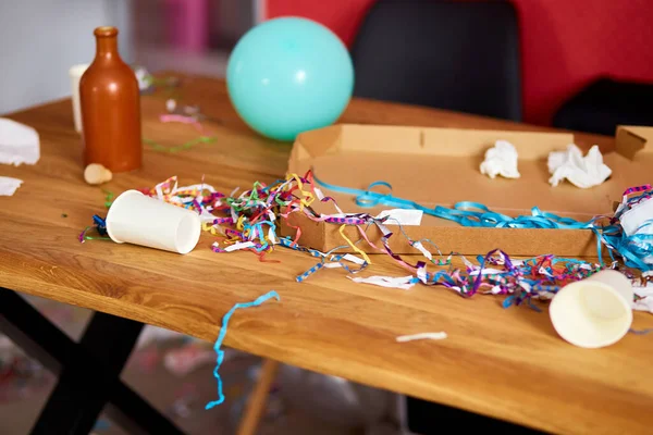 Parti kutlamalarından sonra parti kaosundan sonra parti artıklarını kutlamak için pizza kutusu, boş mavi şişeler, şarap bardağı ve parti süslemeleri olan dağınık ahşap masa..