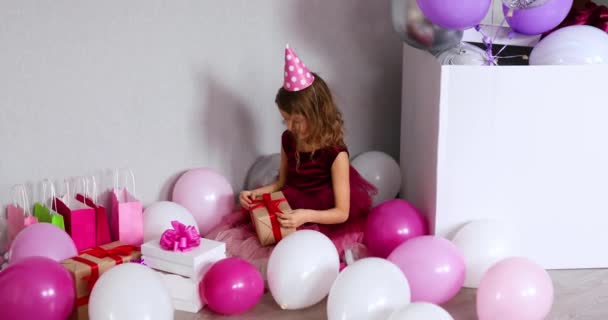 女の子オープニングプレゼントで彼女の誕生日パーティー 好奇心の強い子供は 彼女がすでに受け取った誕生日の贈り物を見て — ストック動画