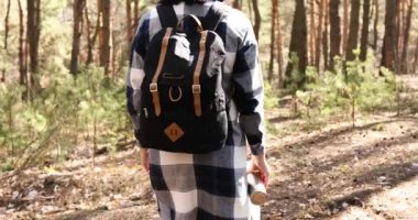 Genç bir kadın çam ormanında çantasıyla yürüyor. Aktif, sağlıklı bir gezgin. Bahar güneşli bir günde ormanda yürüyor.