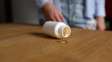 Geri dönüş balık yağı haplarını şişeye ters çevirme videosu, kadının eli, düştükten sonra ahşap masaya dökülen malzemeler, sağlık ve ilaç kavramı,.