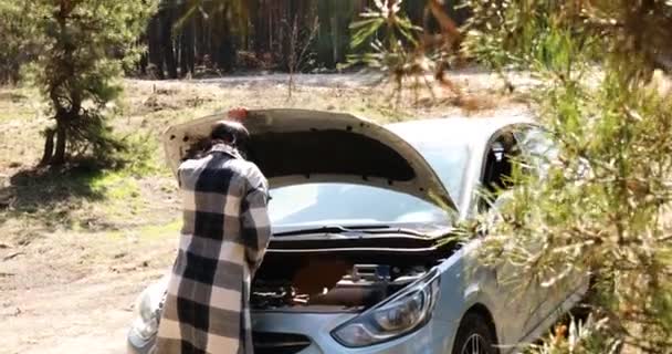 Jovem fêmea que abre o capô do veículo e examina o motor do carro quebrado na estrada florestal — Vídeo de Stock