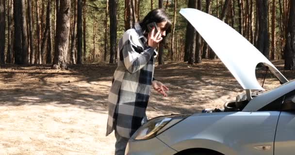 Jonge vrouw met smartphone, bellen auto assistentie diensten in de buurt van het openen van het voertuig kap van gebroken auto — Stockvideo
