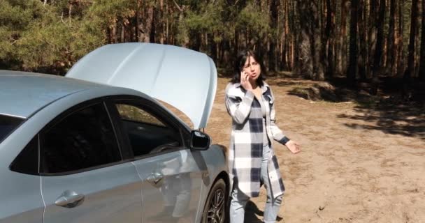 Νεαρή γυναίκα που χρησιμοποιεί το smartphone, καλώντας τις υπηρεσίες βοήθειας αυτοκινήτων κοντά στο άνοιγμα του καπό οχημάτων του σπασμένου αυτοκινήτου — Αρχείο Βίντεο