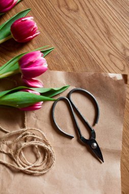 El işi kağıdıyla çiçekli iş yeri, ahşap masa üzerinde pembe lale buketi, hobi, diy, bahar hediyesi konsepti yukarıdan.