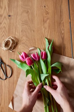 Ahşap masa üzerinde pembe lale buketi düzenleyen kadın elleri, çiçeklerle dolu iş yeri, iş yeri, diy, bahar hediyesi konsepti yukarıdan.