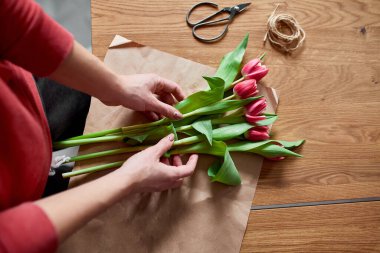 Ahşap masa üzerinde pembe lale buketi düzenleyen kadın elleri, çiçeklerle dolu iş yeri, iş yeri, diy, bahar hediyesi konsepti yukarıdan.