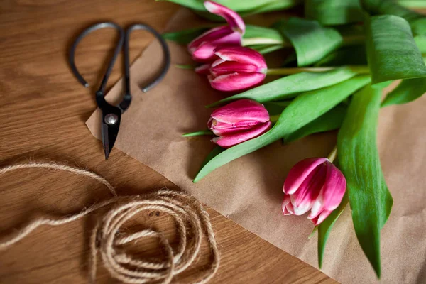 El işi kağıdıyla çiçekli iş yeri, ahşap masa üzerinde pembe lale buketi, hobi, diy, bahar hediyesi konsepti yukarıdan.