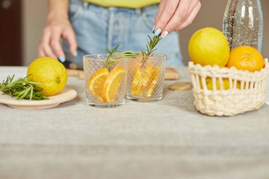 Kadın eli biberiyeyi bardağa, hazırlayan kadın turunçgil ve biberiyeli taze limonatayı evdeki beyaz bir masada, yaz içeceği, sağlıklı su detoksunda yapıyor..