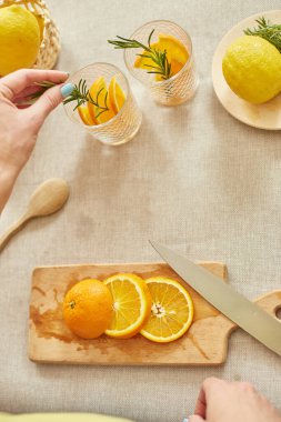 Kadın eli biberiyeyi bardağa, hazırlayan kadın turunçgil ve biberiyeli taze limonatayı evdeki beyaz bir masada, yaz içeceği, sağlıklı su detoksunda yapıyor..