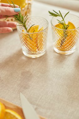 Kadın eli biberiyeyi bardağa, hazırlayan kadın turunçgil ve biberiyeli taze limonatayı evdeki beyaz bir masada, yaz içeceği, sağlıklı su detoksunda yapıyor..