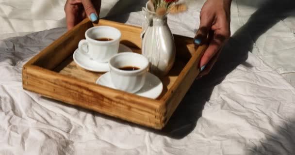 Café da manhã na cama, mãos femininas colocar tentar com duas xícaras de café e flor na luz do sol — Vídeo de Stock