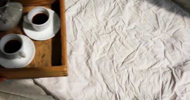 Сніданок в ліжку, жіночі руки ставлять спробувати з двома чашками кави і квітка на сонячному світлі — стокове відео
