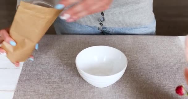 在家里准备健康早餐的女人 将麦片倒入坚果种子葡萄干碗 在家吃燕麦饭 生活方式的概念 — 图库视频影像