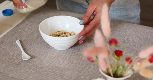 Mão feminina segurando garrafa derramando leite em flocos de granola de cereais tigela — Vídeo de Stock