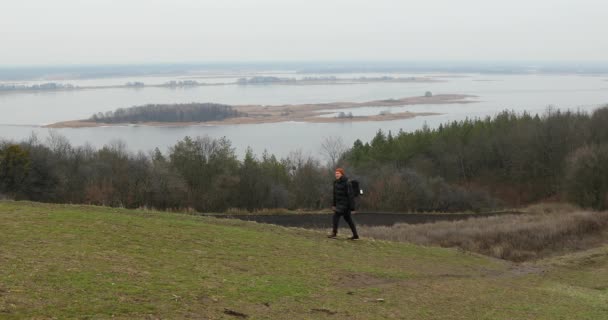 Viajantes caminhantes do sexo masculino com mochila andando ao longo das montanhas contra a vista do rio — Vídeo de Stock