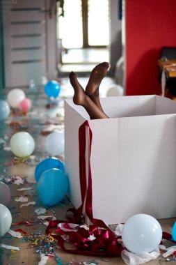 Sızdıran çoraplarla dolu büyük kutudan sarkan kadın bacakları, parti kaosundan sonra, evdeki dağınık oturma odası, konfeti ve balonlar, her sabah parti kutlamaları..