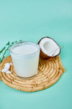 Mavi arka planda bir bardakta taze hindistan cevizi sütü, alternatif türde vegan sütü, organik sağlıklı içecek konsepti..