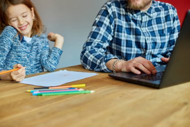 Babası evinde dizüstü bilgisayarla çalışıyor, kızı yanına oturuyor ve kendi başına resim çiziyor, uzaktan çalışıyor ve iş yerinde çocuk büyütüyor..