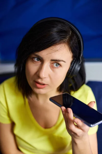 Wesoła Kobieta Luźnych Ubraniach Słuchawkami Smartfonem Nagrywać Podcastu Kanapie Domu — Zdjęcie stockowe