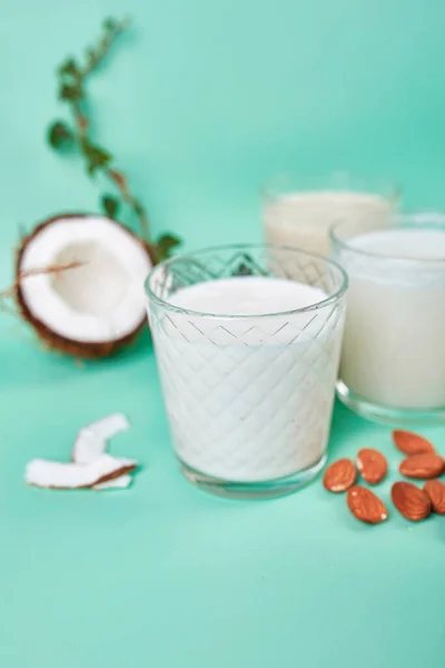 Various vegan plant based milk and ingredients, non-dairy milk, alternative types of vegan milks in glasses on a blue background with copy space