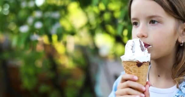 Linda chica comiendo helado italiano cono sonriendo mientras descansa en el parque en el día de verano — Vídeos de Stock