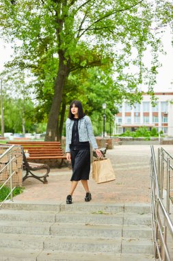 Elinde bir kaç kese kâğıdı olan bir kadın. Parkta yürürken, alışveriş yaptıktan sonra..