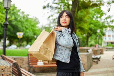 Elinde bir kaç kese kâğıdı olan bir kadın. Parkta yürürken, alışveriş yaptıktan sonra..