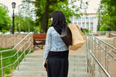 Elinde bir kaç kese kâğıdı olan bir kadın. Parkta yürürken, alışveriş yaptıktan sonra..