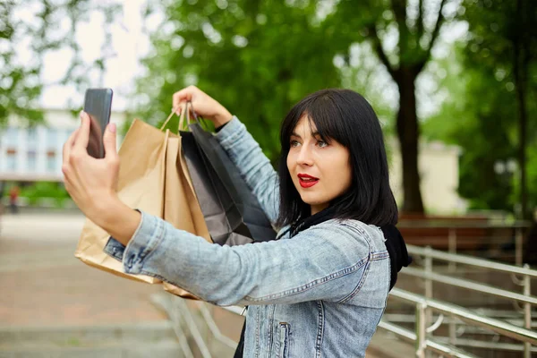 Brunetka Kobieta Trzyma Papierowe Torby Zakupy Robi Selfie Przez Smartfona — Zdjęcie stockowe