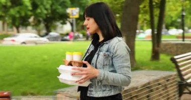 Parkta yürüyen bir kadın, elinde yiyecek ve kahve, işten öğle yemeği molası..